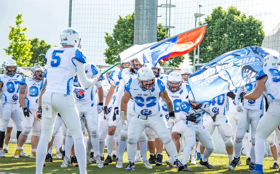 Igrači američkog fudbala Blue Dragons u belim i plavim dresovima izlaze na teren sa zastavama